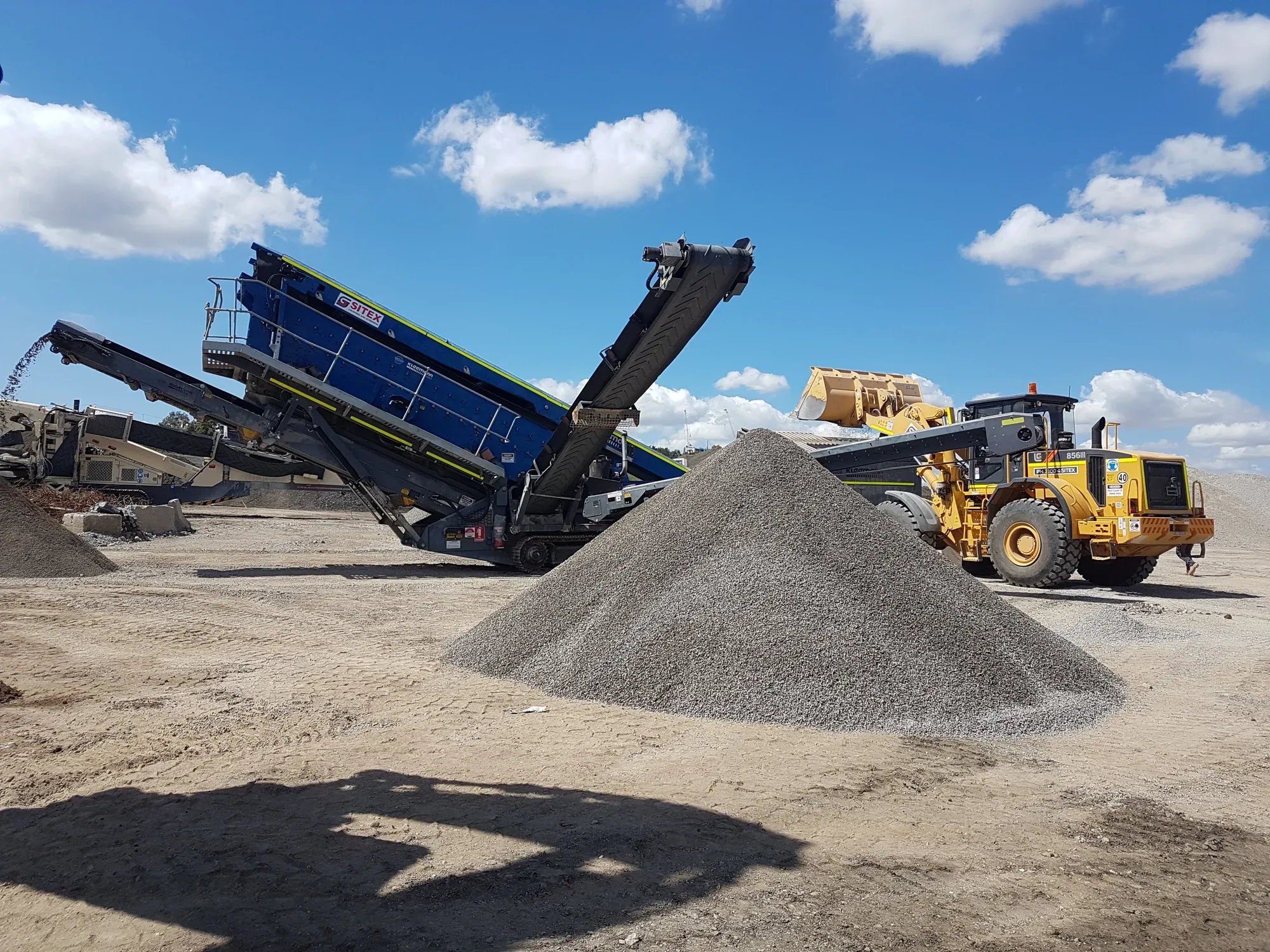 Loader working graded product beside a mobile screen